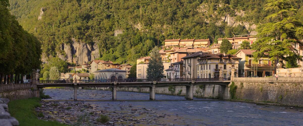 A river with a stone bridge, buildings, and a mountainous backdrop.