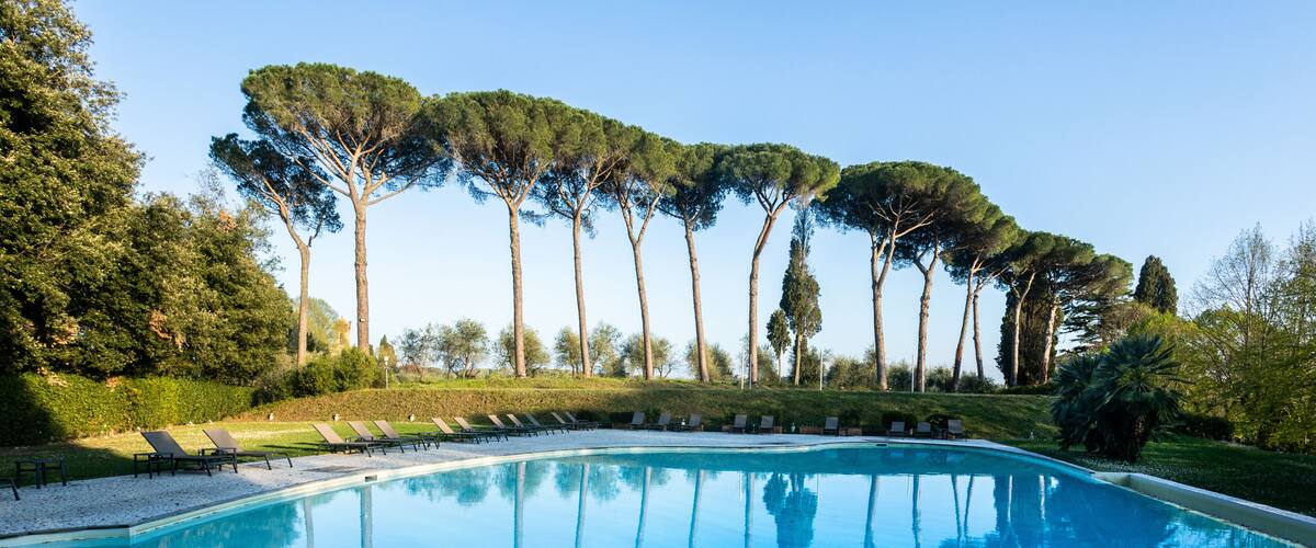 A swimming pool with lounge chairs and tall trees in the background.
