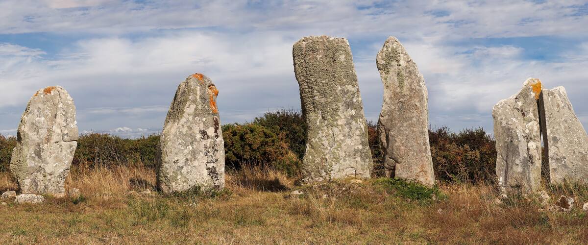 Five standing stones in a grassy field with a cloudy sky.
