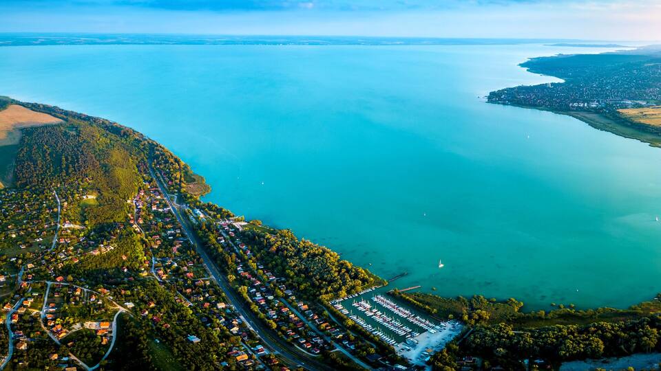An aerial view of a coastal town with a marina, surrounded by green fields and a large body of water.