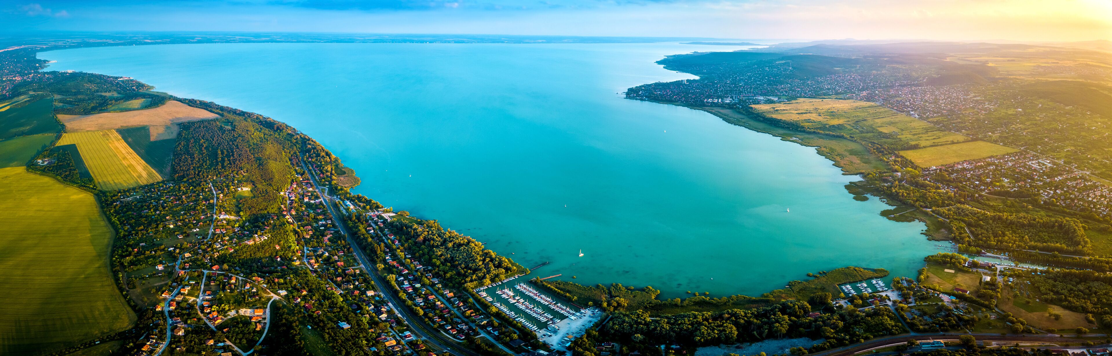 An aerial view of a coastal town with a marina, surrounded by green fields and a large body of water.