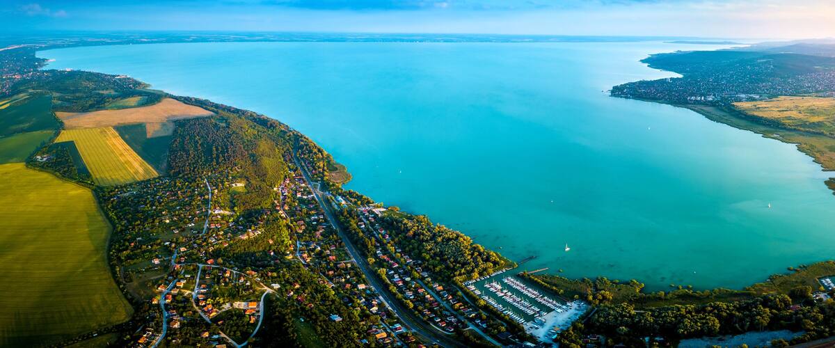An aerial view of a coastal town with a marina, surrounded by green fields and a large body of water.