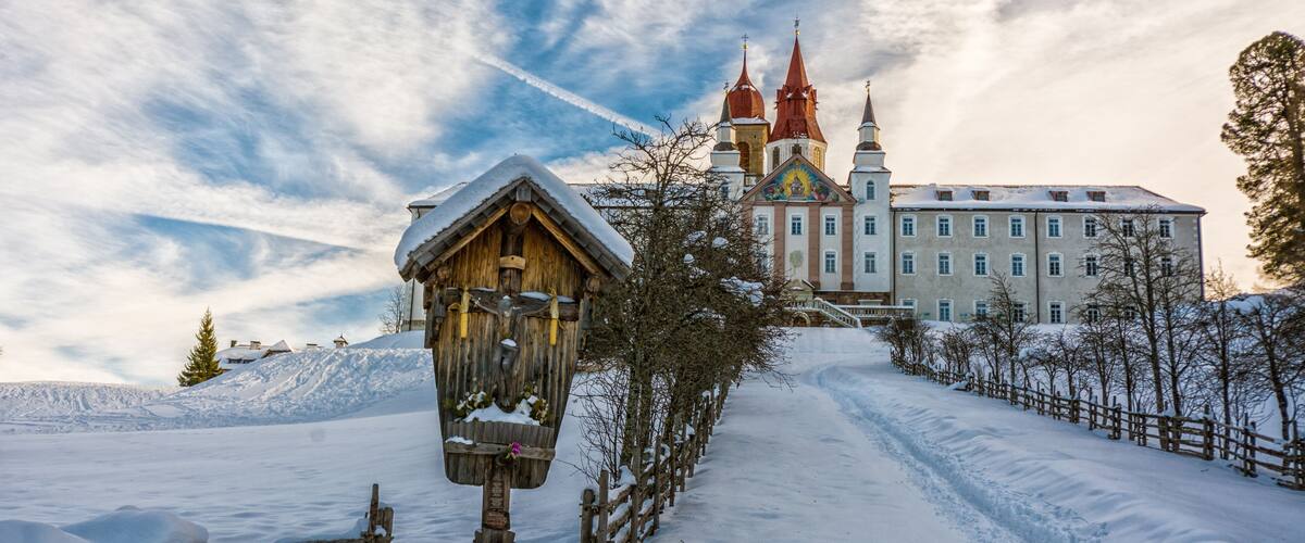 A wooden structure with a snow-covered roof, a large building with red spires, and a snow-covered landscape.