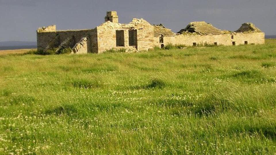 A dilapidated stone building in a grassy field.