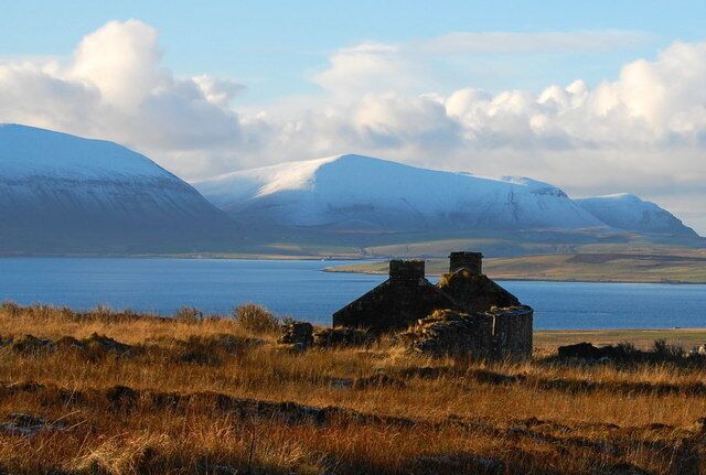 A lake with mountains in the background and a ruined structure in the foreground.