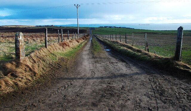 Track to the A964 The A road is hidden in the dip. The lane continues down to Smoogro, with Scapa Flow (and oil tankers) beyond.
