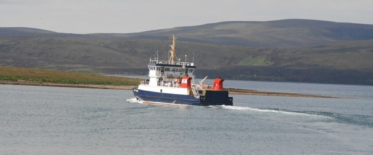 A ferry moving across a calm body of water with a hilly landscape in the background.