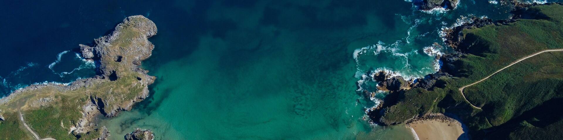 A coastal landscape with a sandy beach, clear turquoise waters, and rocky cliffs.