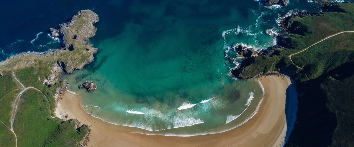 A coastal landscape with a sandy beach, clear turquoise waters, and rocky cliffs.