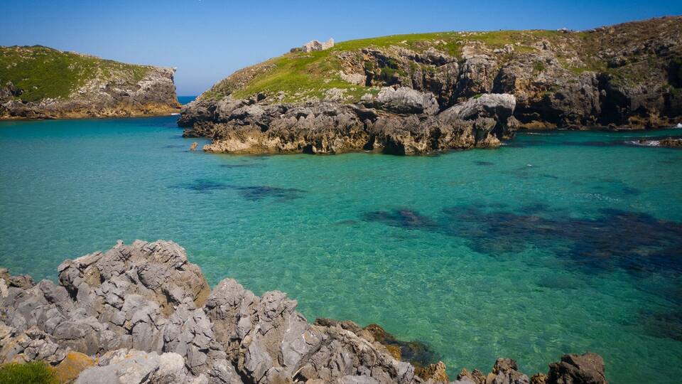 A coastal landscape with rocky cliffs and clear turquoise waters.