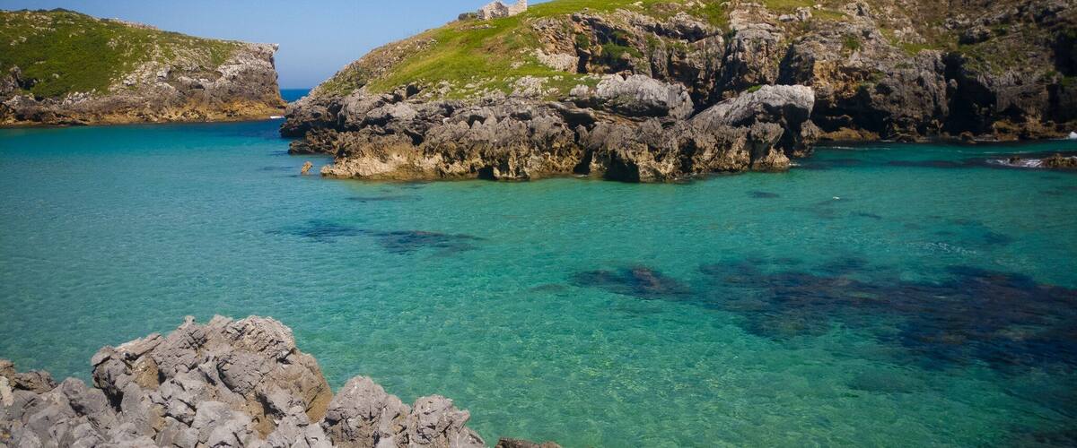A coastal landscape with rocky cliffs and clear turquoise waters.