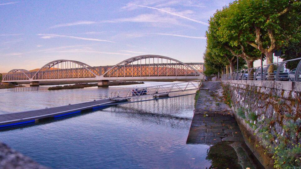 A steel bridge over a river with a pedestrian walkway and a blue boat dock.