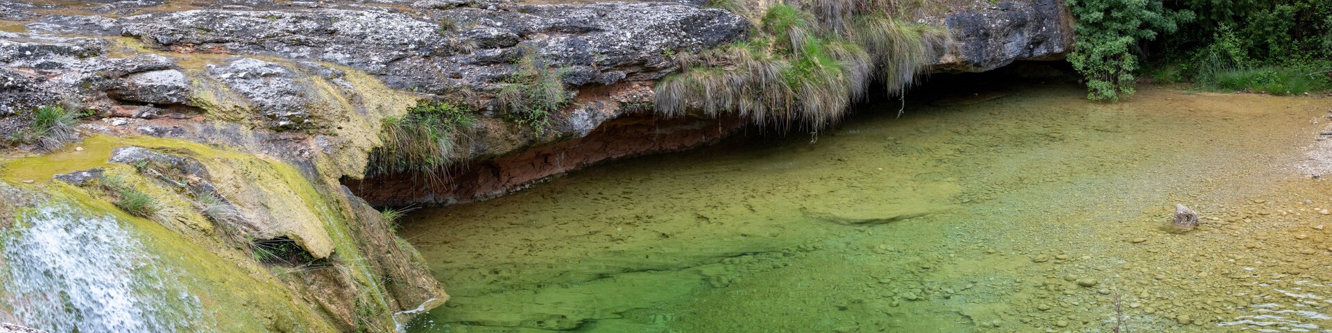 A waterfall flowing over rocks into a green pool surrounded by dense greenery.