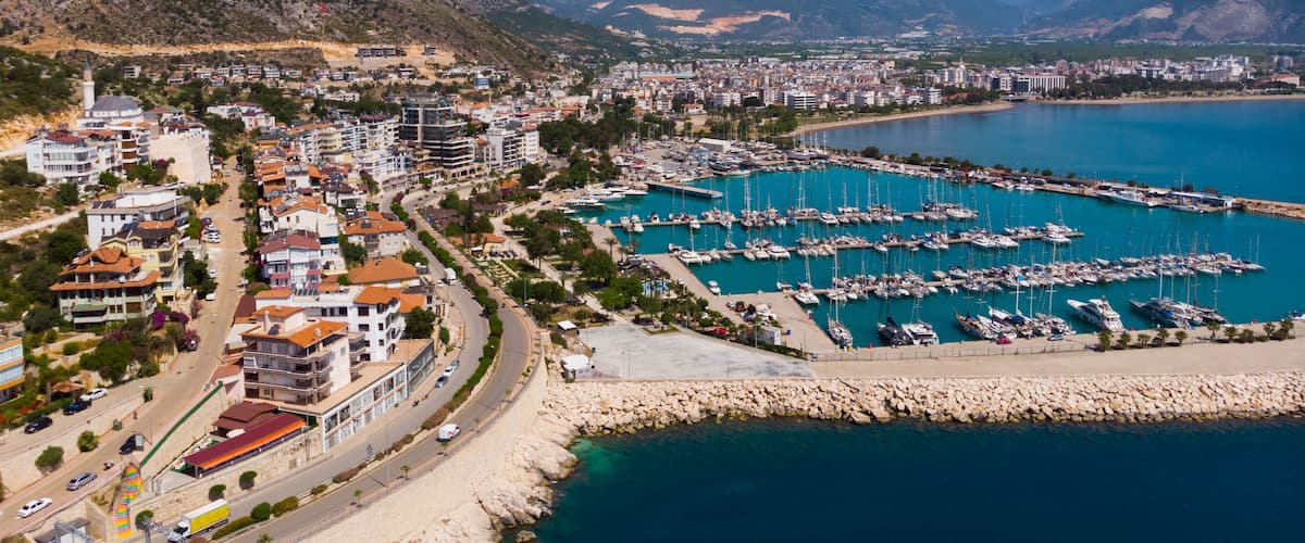 A coastal city with a marina, mountains in the background, and a clear blue sky.