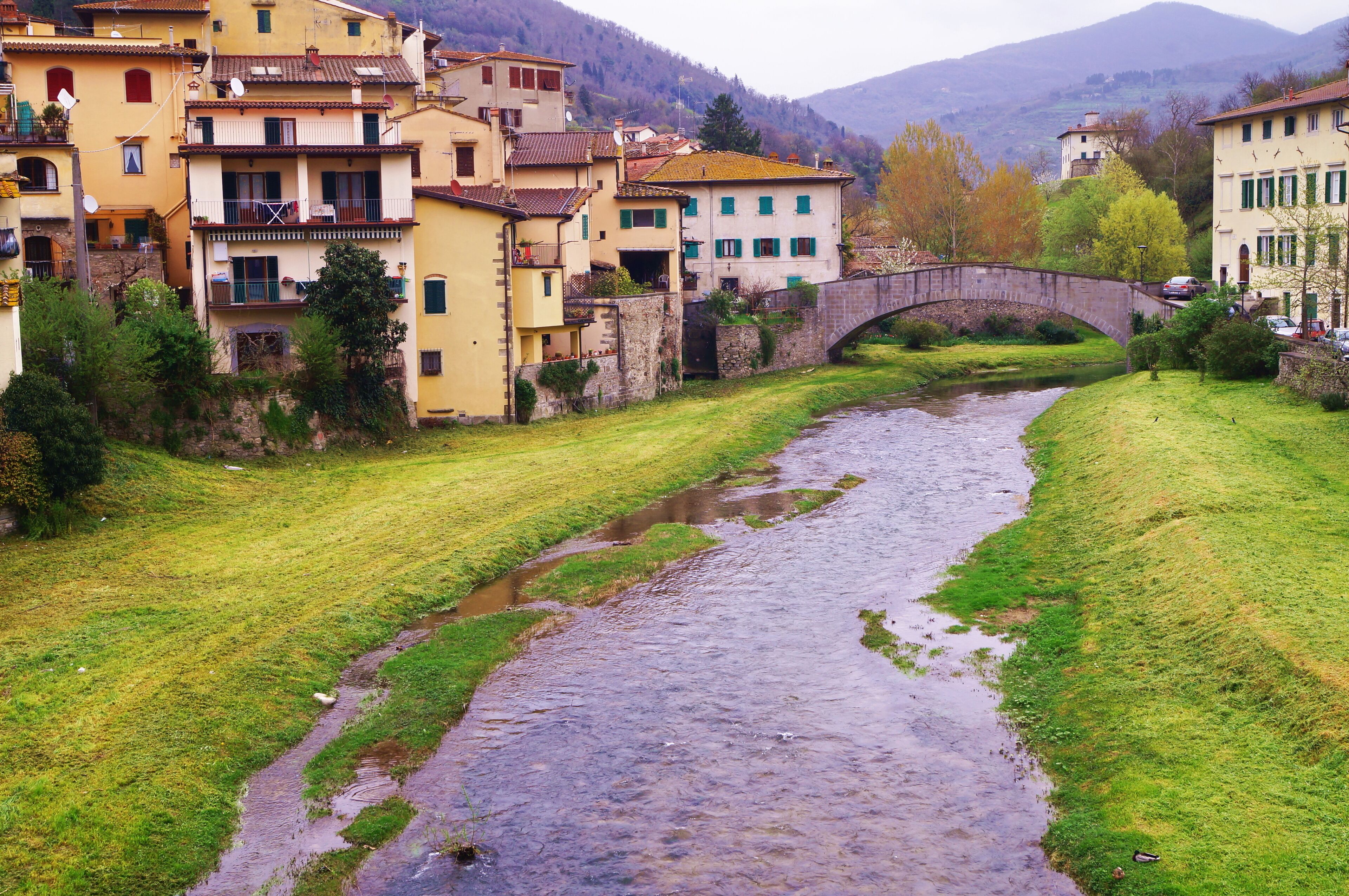 A river flowing through a town with buildings and a stone bridge.