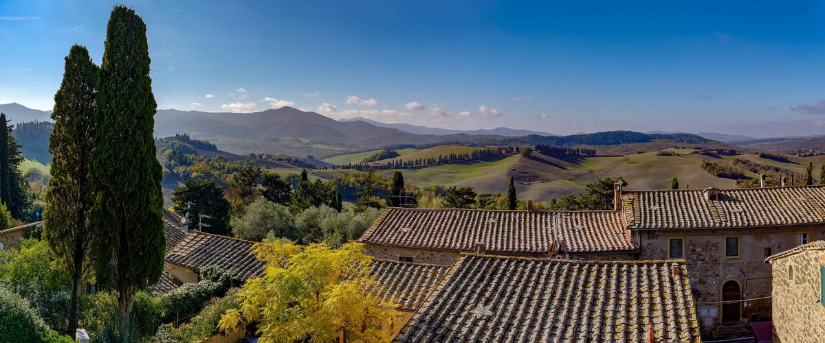 A rural landscape with rolling hills, a tall cypress tree, and traditional tiled-roof buildings.