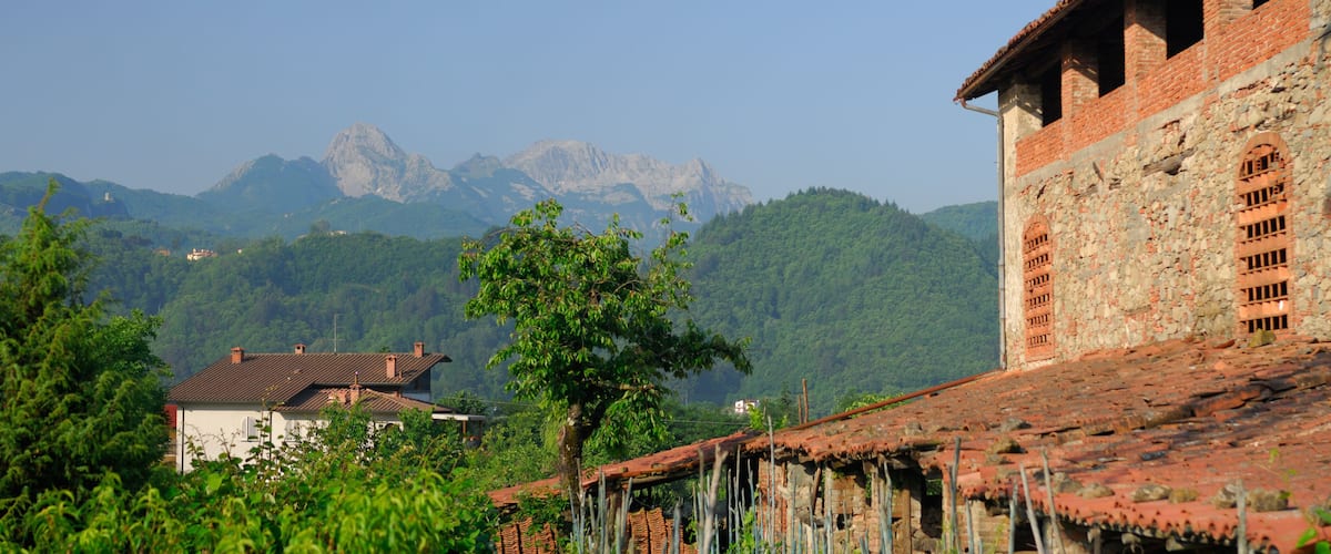 A rural village with traditional stone buildings, lush greenery, and mountains in the background.