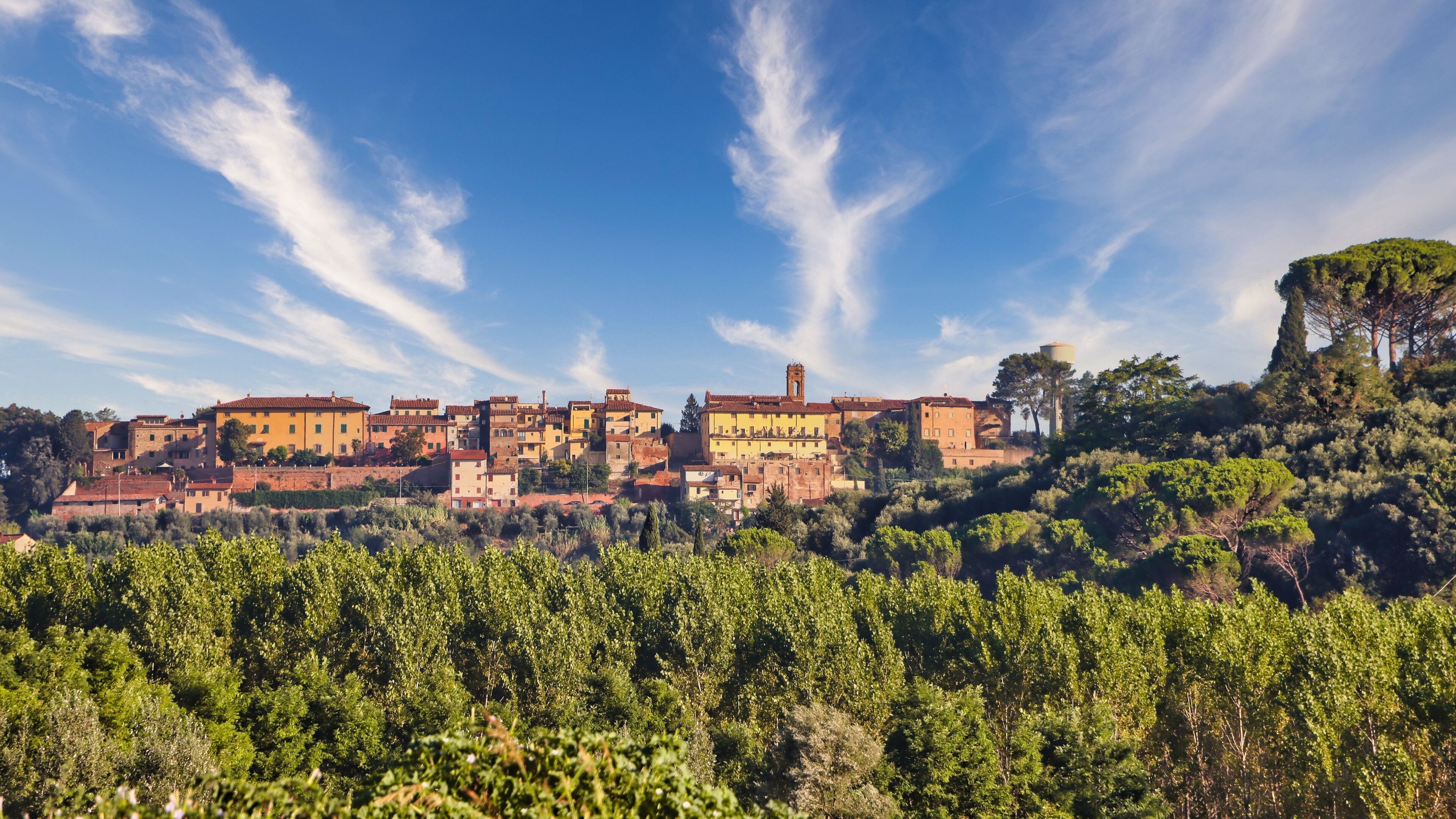 A hillside village with terracotta-roof buildings, a prominent bell tower, and lush greenery.