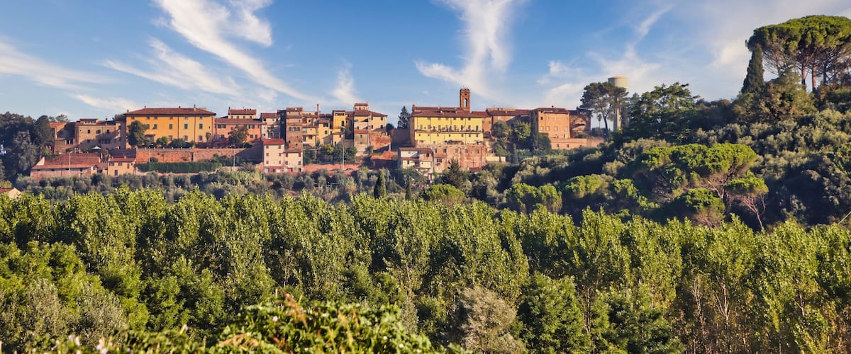 A hillside village with terracotta-roof buildings, a prominent bell tower, and lush greenery.