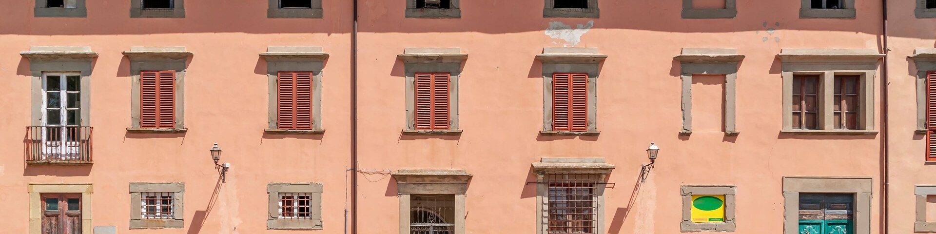 Un edificio rosa con varias ventanas y contraventanas, una puerta verde y un balcón pequeño.