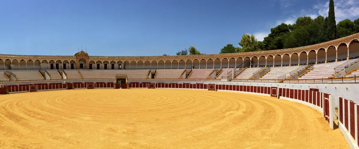 A large, empty bullring with a sandy floor and red and white walls.