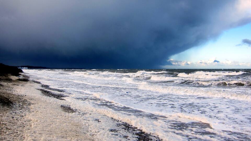 A beach with rough waves and a dark, stormy sky.