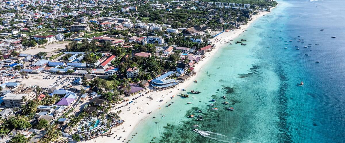 Vista aérea de un pueblo costero con playa, aguas turquesas cristalinas y numerosos barcos.