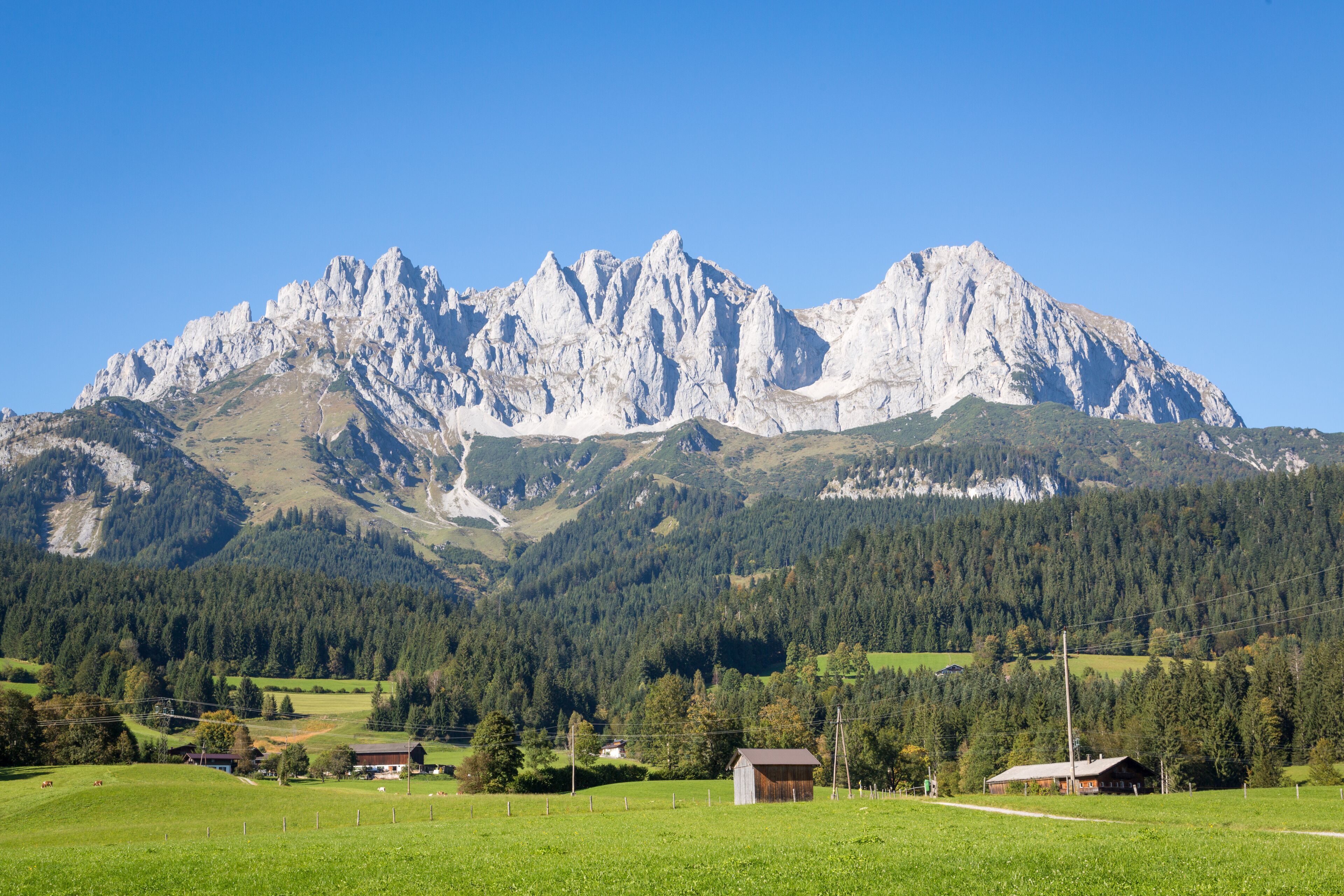 Una cordillera con cielo despejado, campos verdes y pequeñas construcciones.