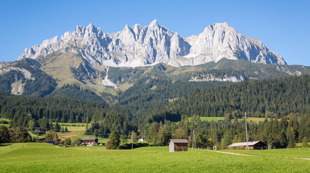Una cordillera con cielo despejado, campos verdes y pequeñas construcciones.