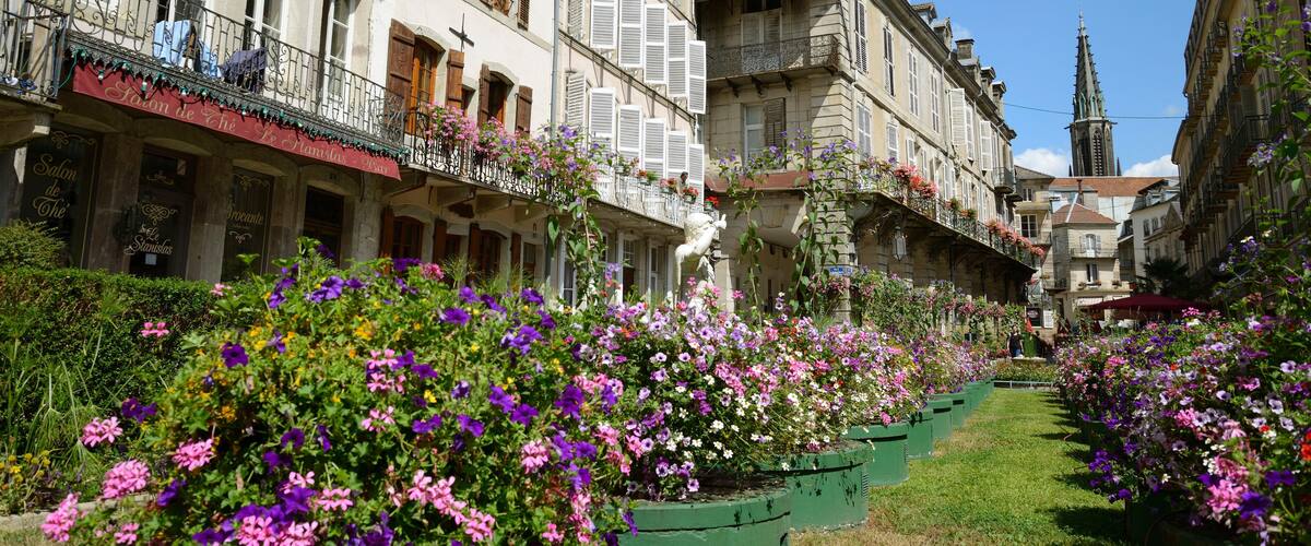 A street lined with colorful flowers, historic buildings, and a church spire.