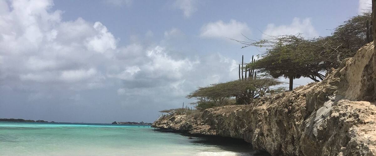 A beach with clear turquoise water, rocky outcrops, and sparse vegetation.