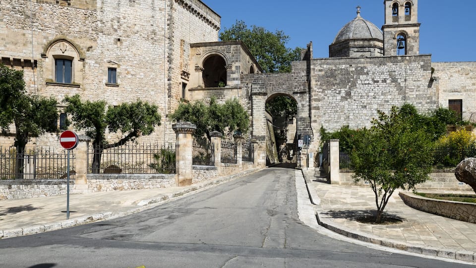 A stone gate leading to a historic building with a bell tower.