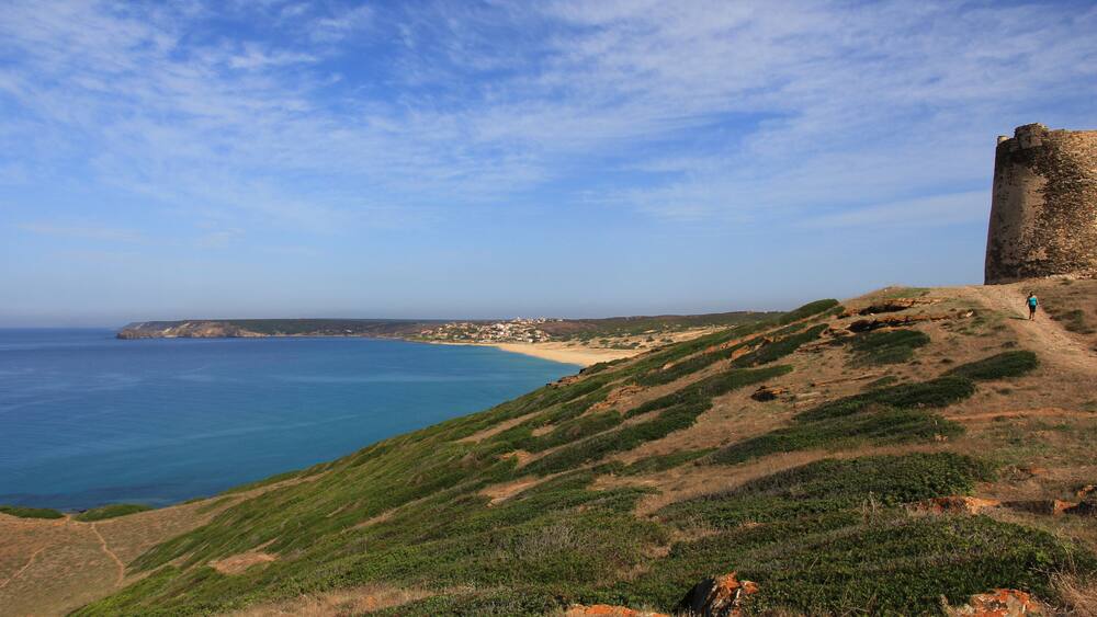 Un paysage côtier avec un château perché sur une colline, une plage et l’océan.