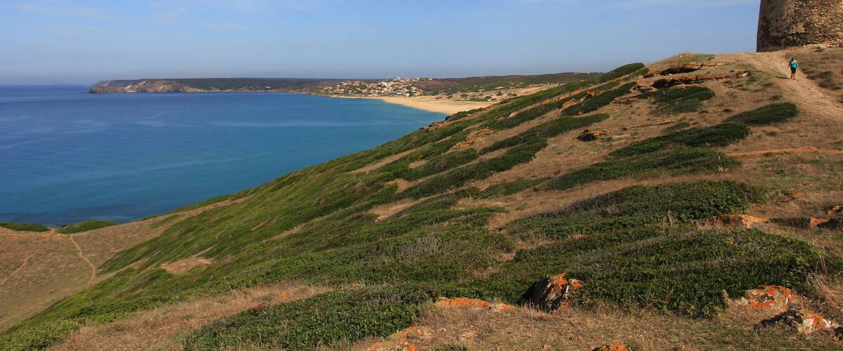 A coastal landscape with a castle on a hill, a beach, and the ocean.