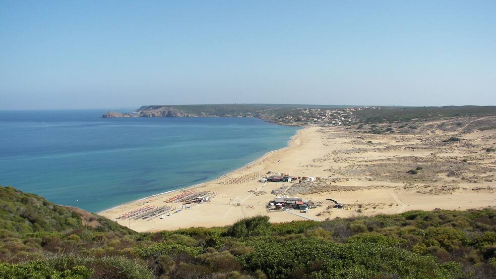 Eine Küstenlandschaft mit Sandstrand, blauem Meer und hügeliger Kulisse.