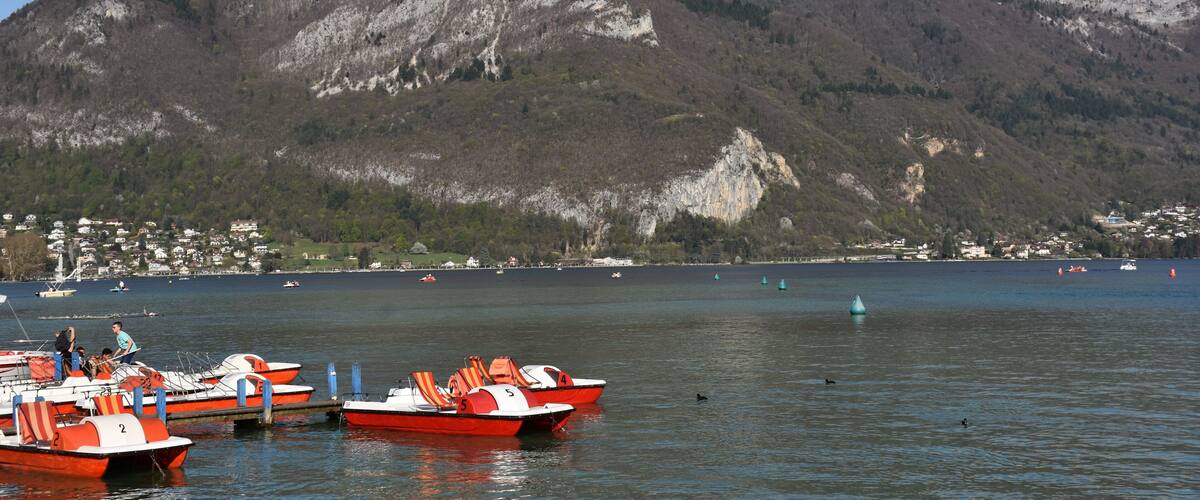 A lake with several small boats docked near the shore, surrounded by a mountainous landscape.