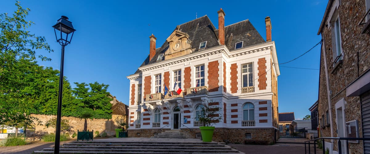A historic building with a clock tower, a flag, and a cobblestone courtyard.