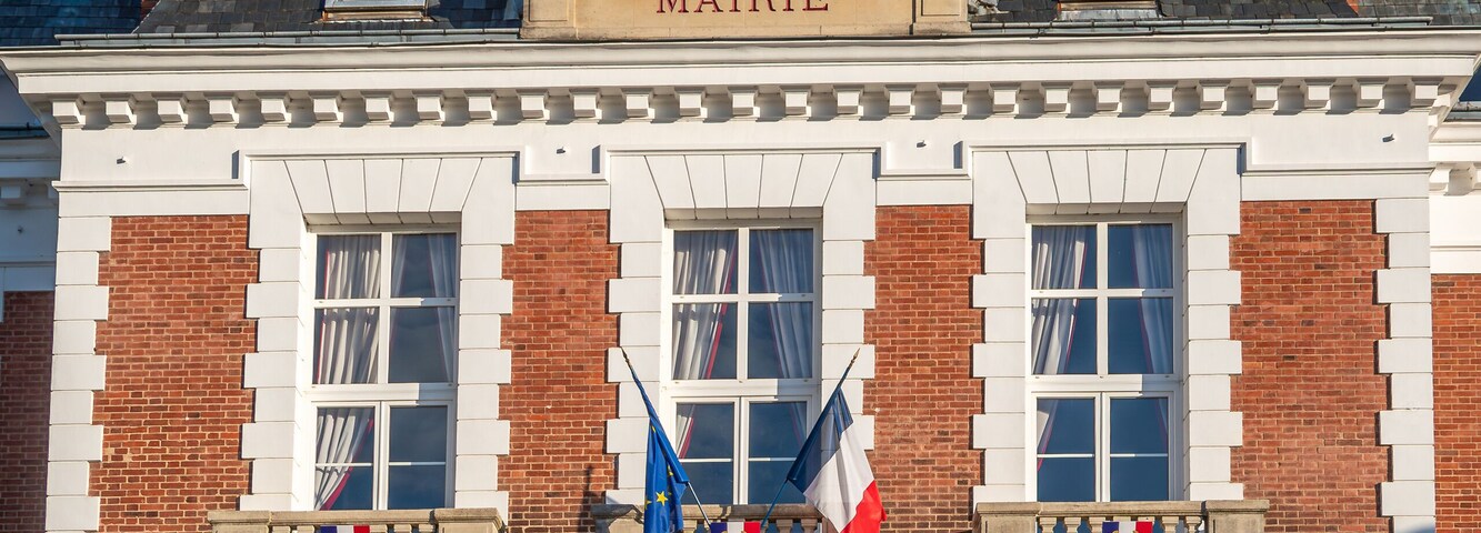 Un edificio histórico con una torre de reloj, llamado "MAIRIE", que presenta un estilo arquitectónico clásico con detalles de ladrillo rojo y piedra blanca.
