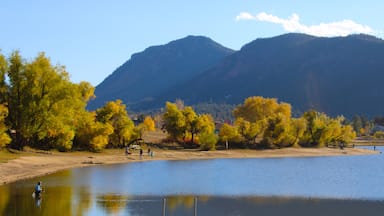 Un lac bordé d’arbres aux couleurs automnales, une plage de sable et des montagnes en arrière-plan.
