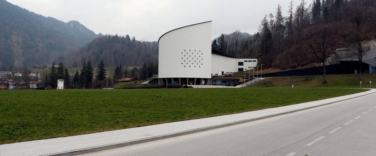A modern building with a unique curved design, set against a backdrop of mountains and a clear road.