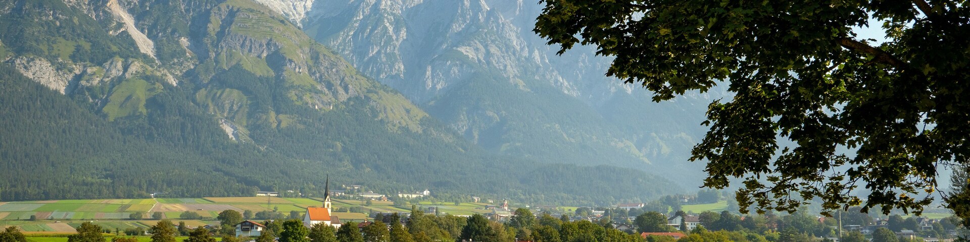A rural landscape with a church, fields, and mountains in the background.
