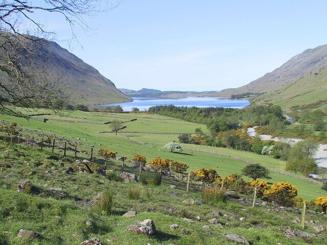 A mountainous landscape with a lake, green fields, and a fence.