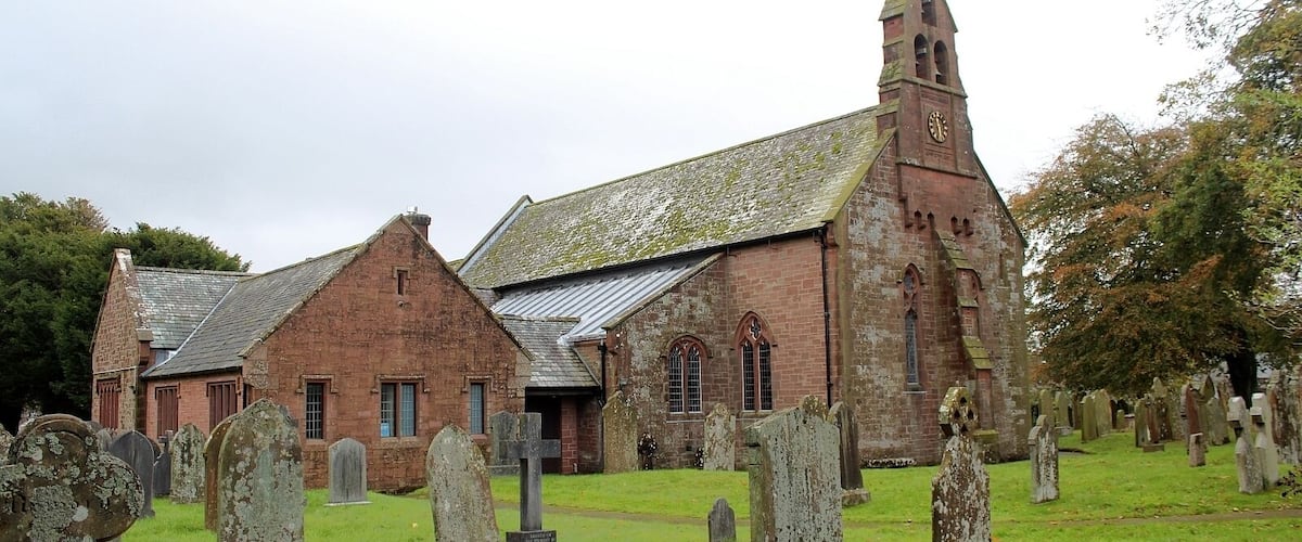 A historic church with a tall steeple and a graveyard in front.