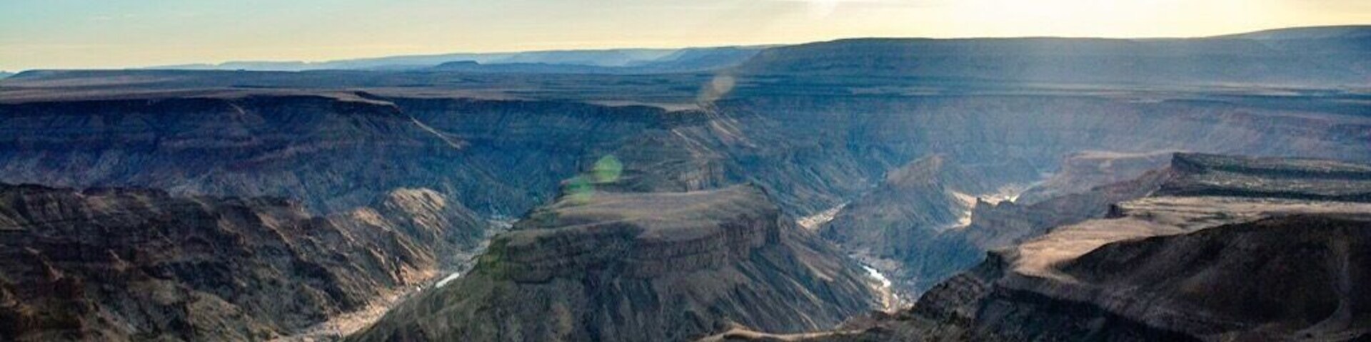 Un vasto cañón con formaciones rocosas estratificadas y un río que lo atraviesa.