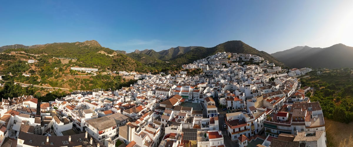 A coastal town with white buildings, terraced hills, and a clear sky.