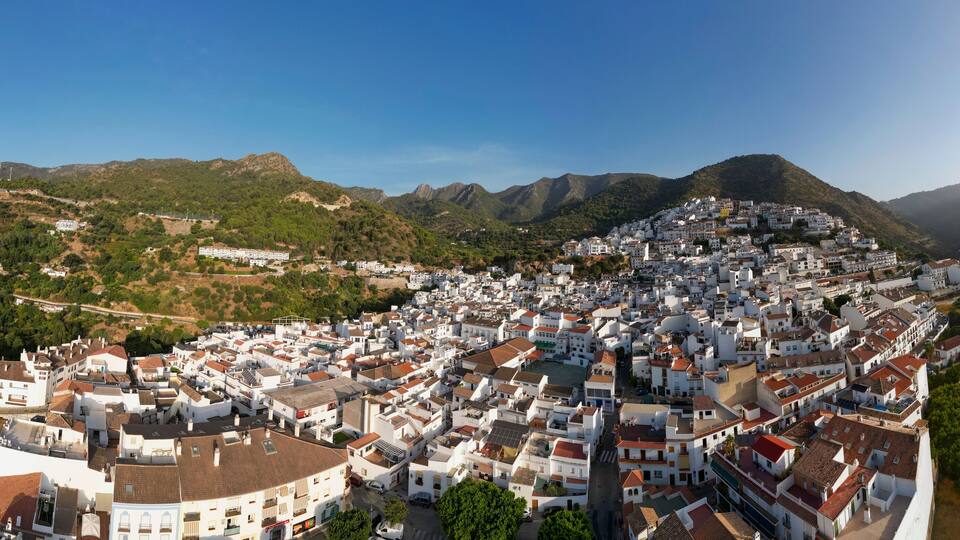 A town nestled in a valley with white buildings and green hills in the background.