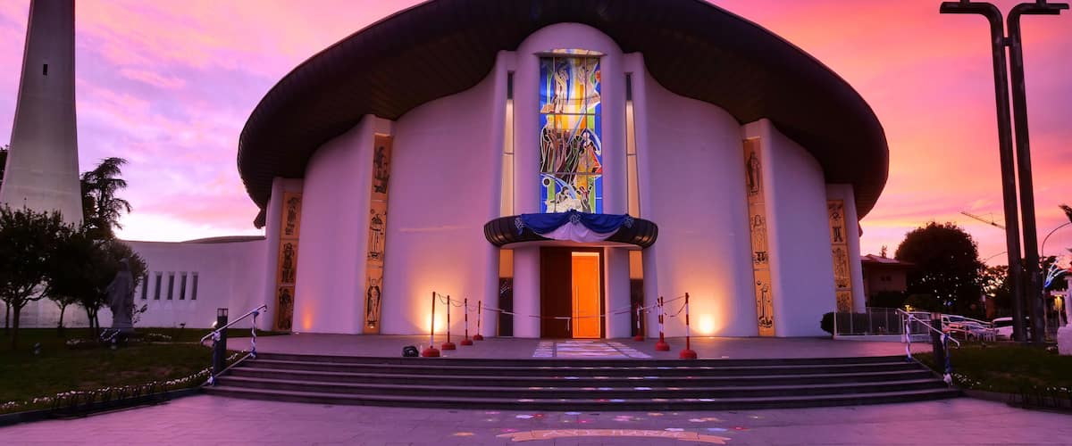 A church with a tall steeple, a large stained glass window, and a cross in front.