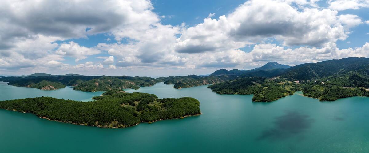 A lake surrounded by forested islands and mountains under a partly cloudy sky.