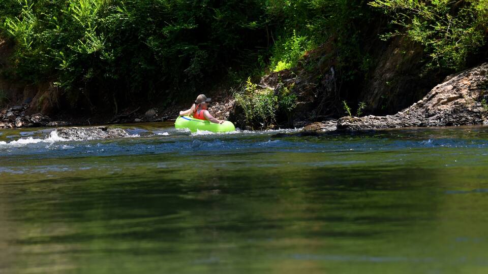 A person kayaking on a river surrounded by dense greenery and rocky terrain.