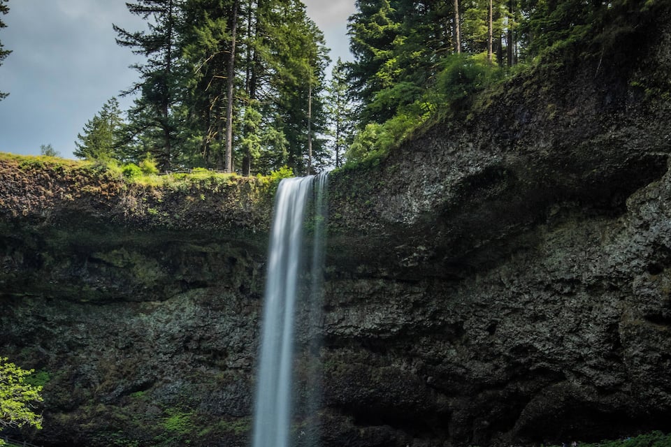 A waterfall cascading into a river surrounded by dense forest and rocky cliffs.